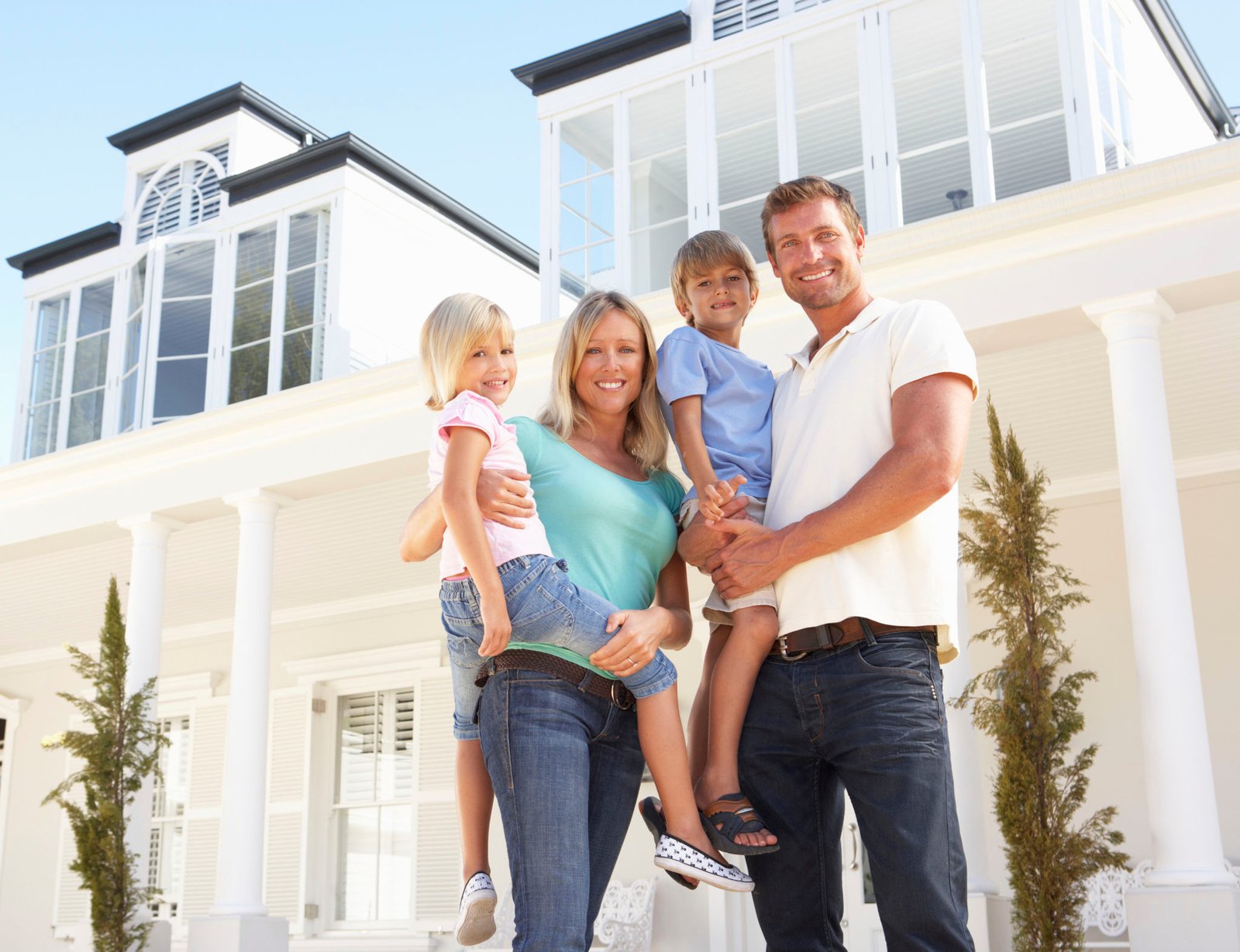 Family standing in front of new home while For Sale sign